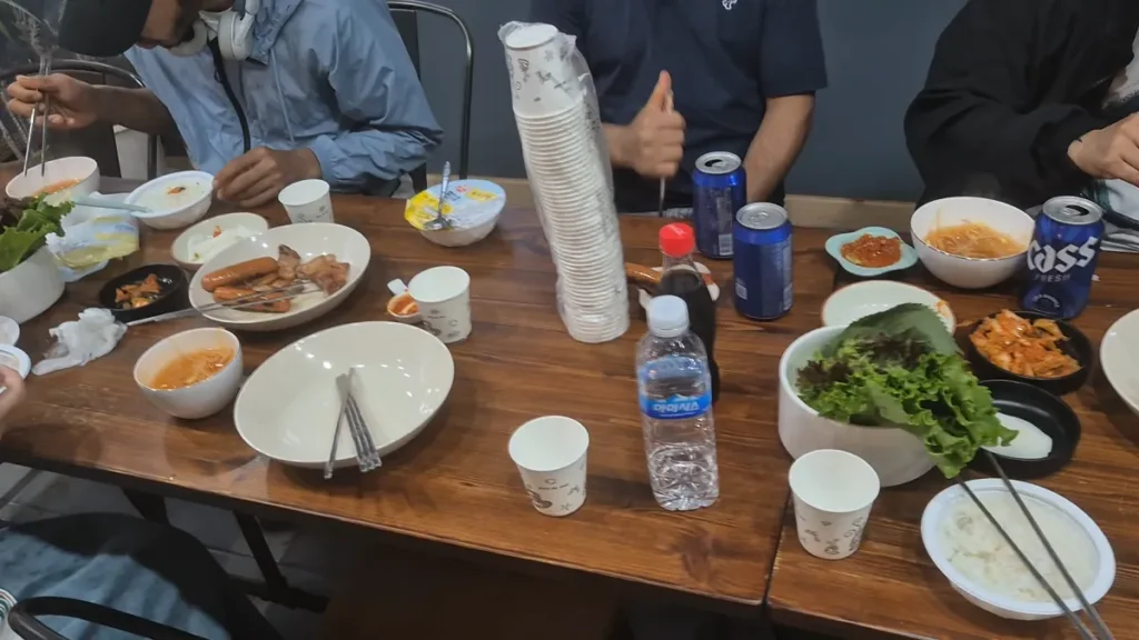 A Korean pension barbecue dinner with grilled meat, side dishes, drinks, and family gathered around the table.